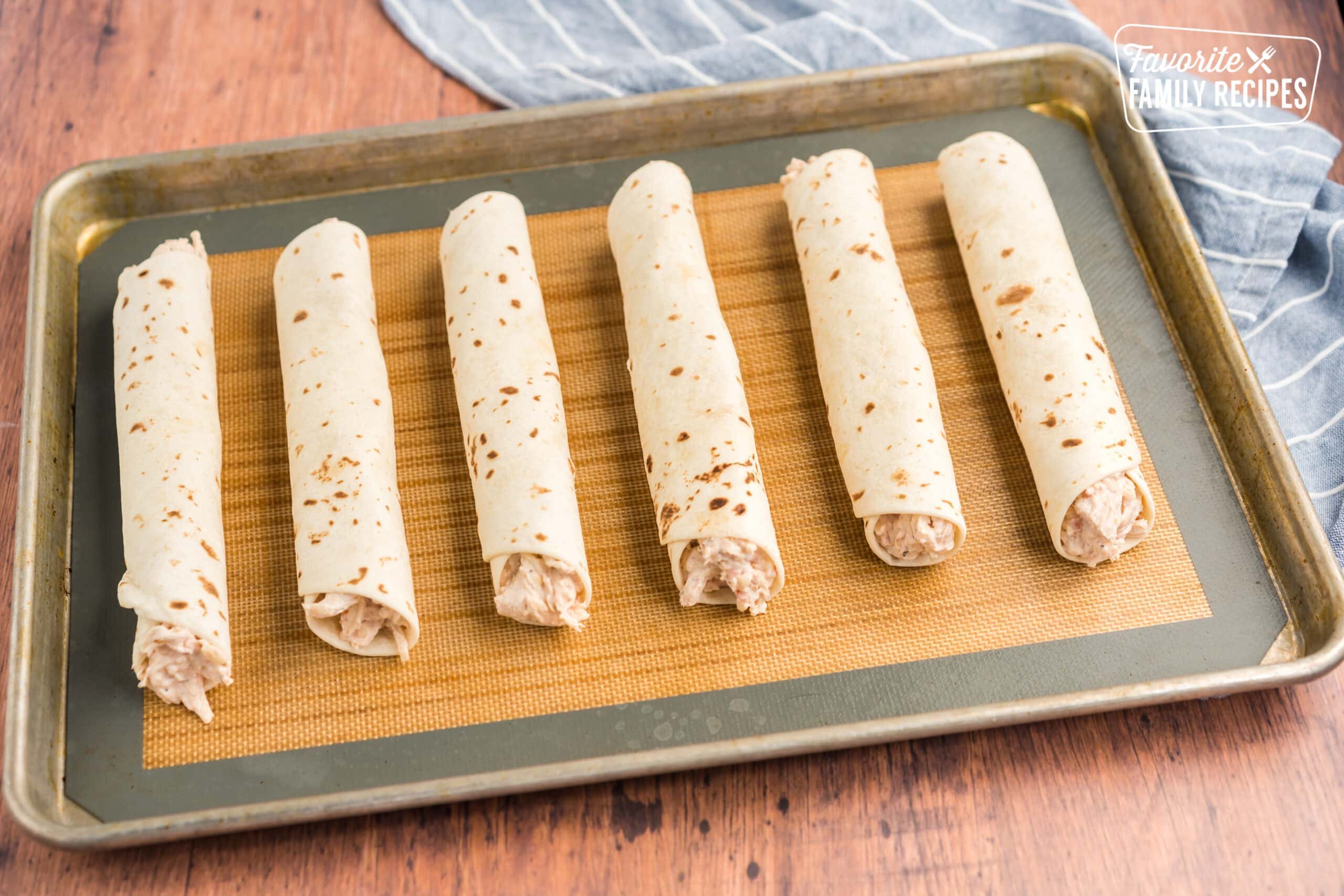 Chicken flautas rolled up on a baking sheet.