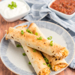 Three chicken flautas on a plate with sour cream and salsa