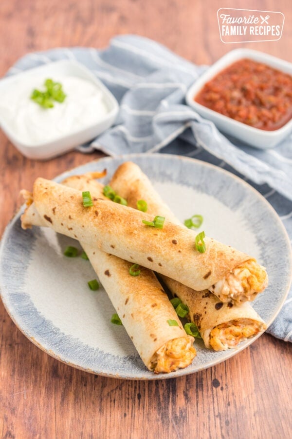 Three chicken flautas on a plate with sour cream and salsa