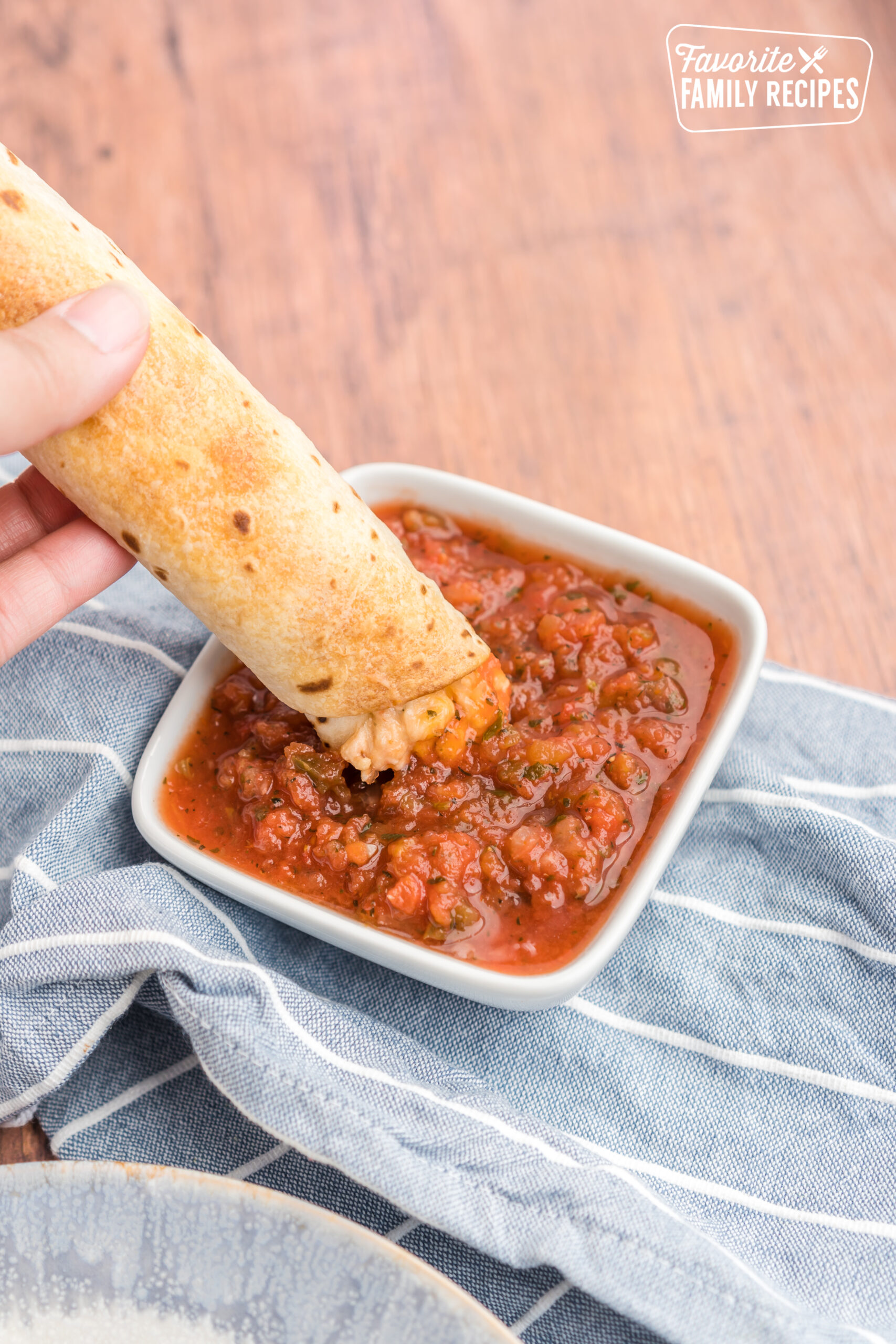 A chicken flauta being dipped in salsa.