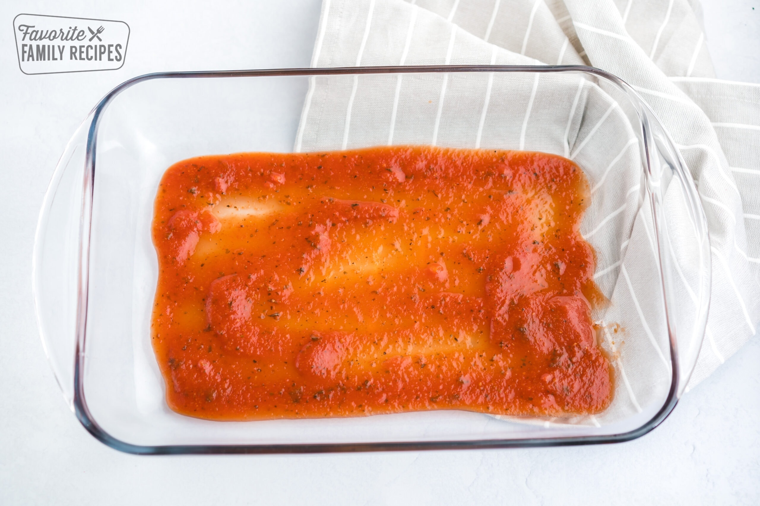 Red sauce on the bottom of a glass pan for the cheese manicotti recipe.