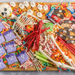 A halloween charcuterie board covered in candy and spooky treats with a skeleton in the middle.