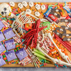 A halloween charcuterie board covered in candy and spooky treats with a skeleton in the middle.
