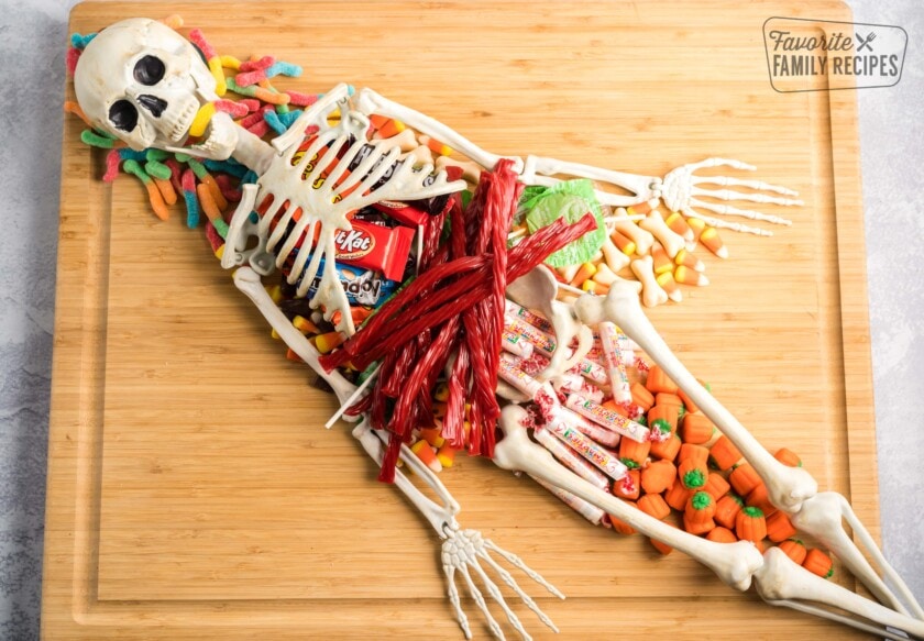 A skeleton on a wooden charcuterie board filled with candy.