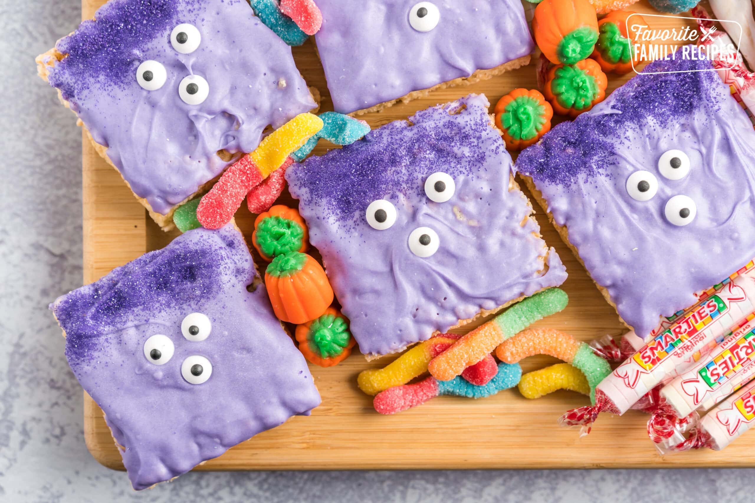 Monsters made out of Rice Krispie Treats dipped in purple chocolate with candy eyes and sprinkles for hair and placed on a Halloween Charcuterie Board. 