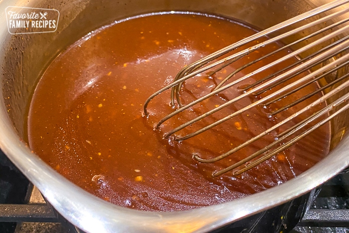 Garlic whisked into honey BBQ sauce in a saucepan