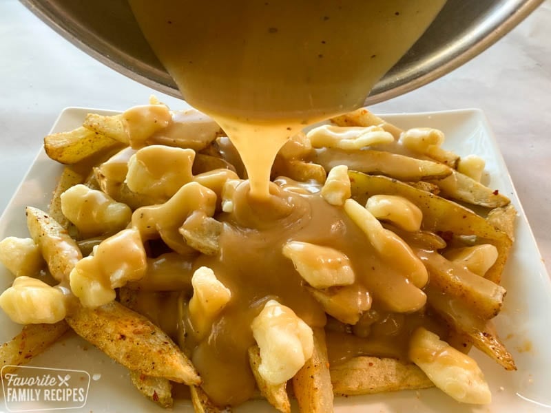 Poutine gravy being poured onto fries.