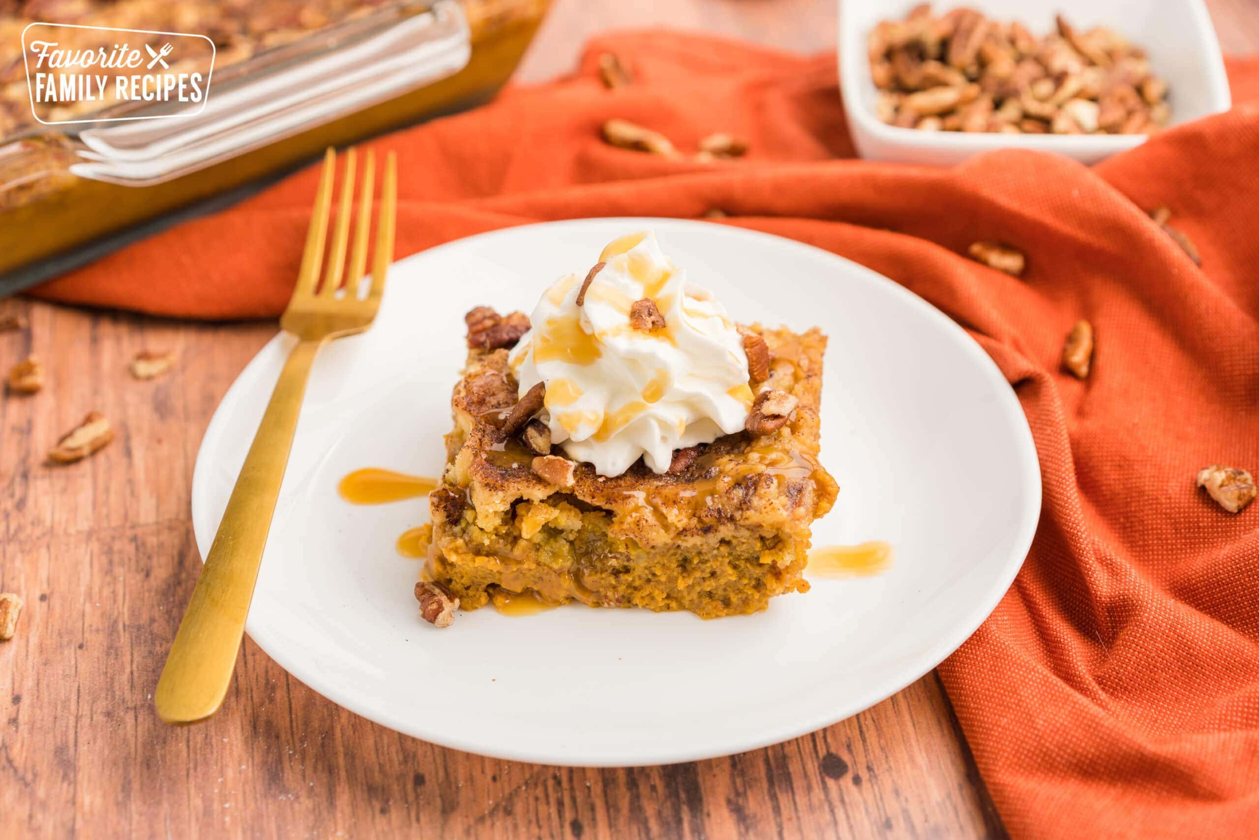 A piece of pumpkin cobbler on a plate topped with whipped cream, caramel, and pecans.