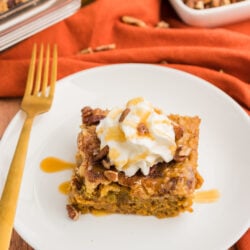 Pumpkin cobbler on a plate topped with whipped cream, caramel sauce, and pecans