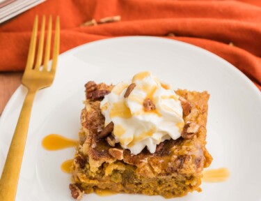 Pumpkin cobbler on a plate topped with whipped cream, caramel sauce, and pecans