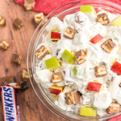 Snickers salad in a glass bowl with pieces of snickers on the side.