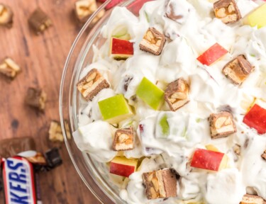 Snickers salad in a glass bowl with pieces of snickers on the side.