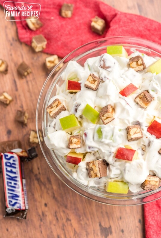 Snickers salad in a glass bowl with pieces of snickers on the side.