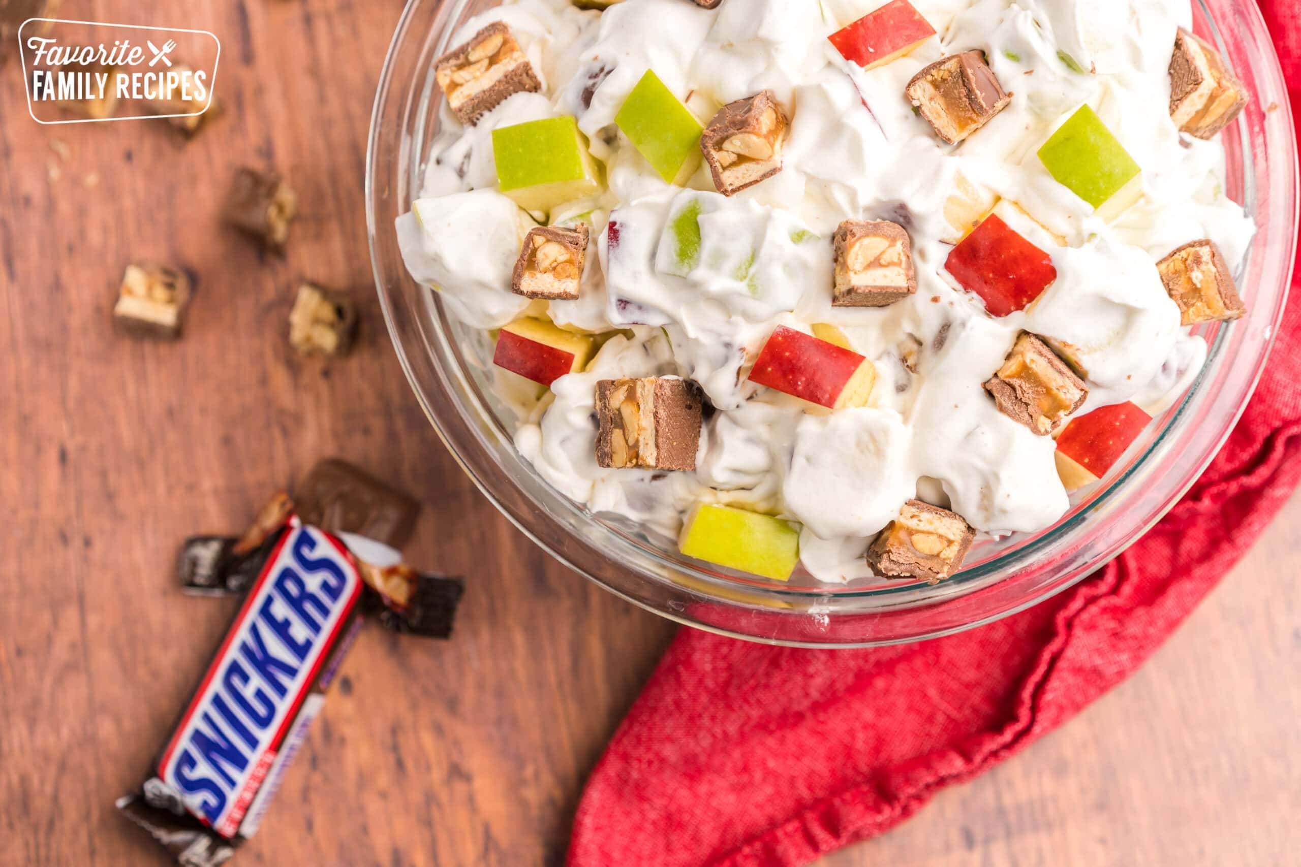 Snicker apple salad in a glass bowl with a snickers bar on the table next to it.