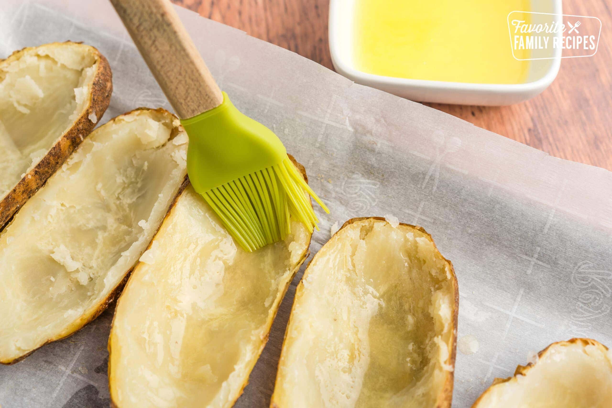 Potato skins being brushed with melted butter to make twice baked potatoes