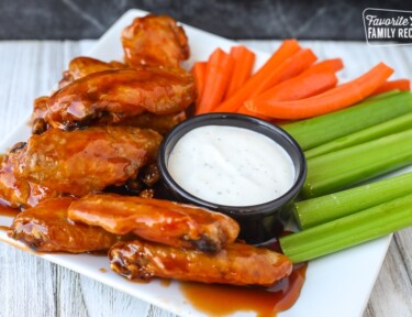 Side view of air fryer chicken wings on a plate with veggies and ranch dip