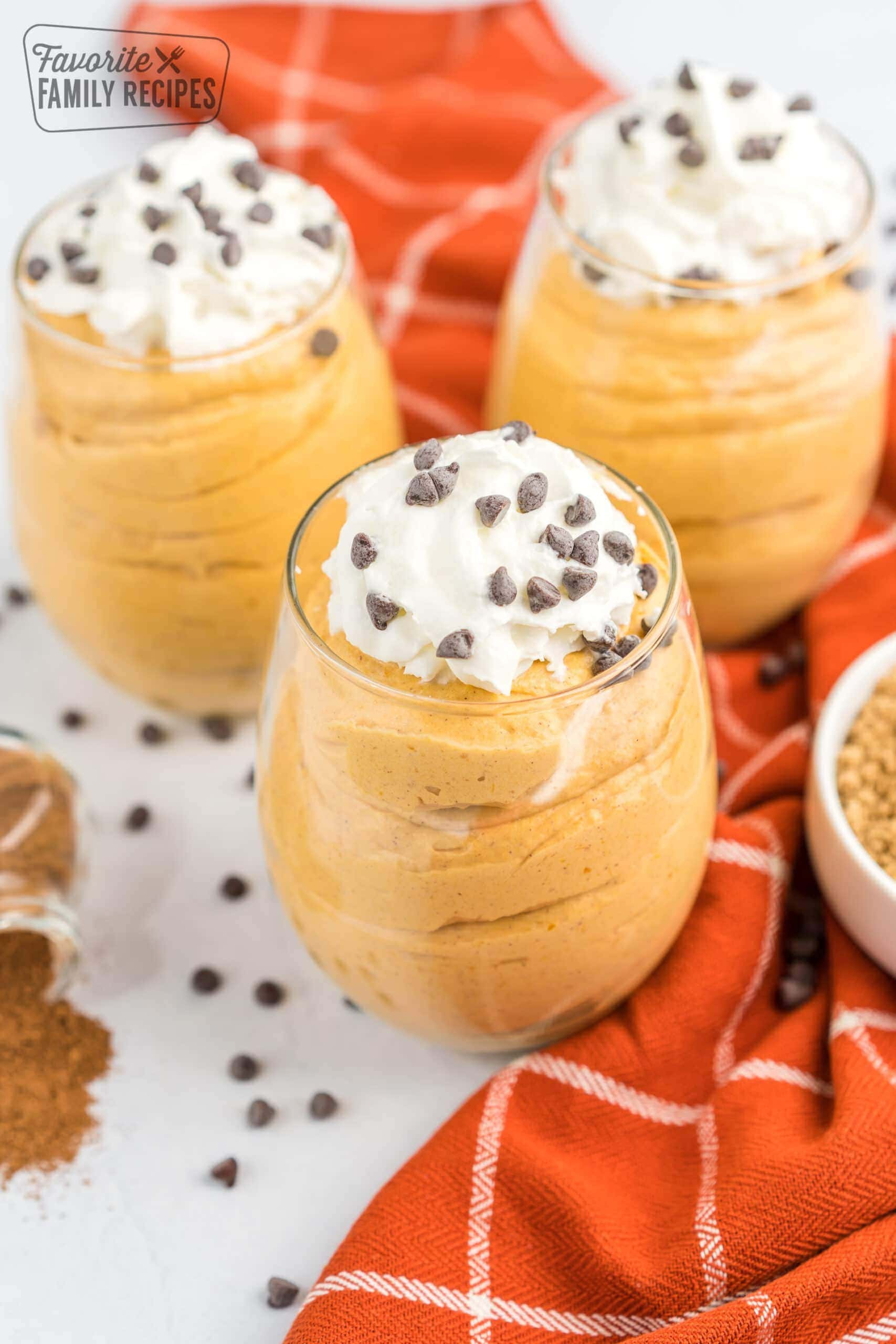 Three cups of pumpkin mousse topped with whipped cream and chocolate chips.