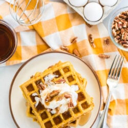 A stack of pumpkin waffles topped with whipped cream, pecans, and syrup.