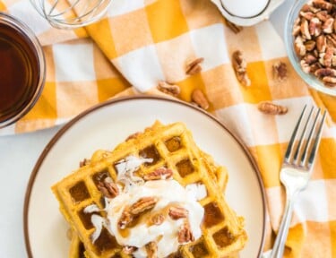 A stack of pumpkin waffles topped with whipped cream, pecans, and syrup.