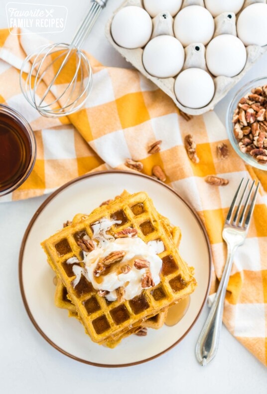 A stack of pumpkin waffles topped with whipped cream, pecans, and syrup.