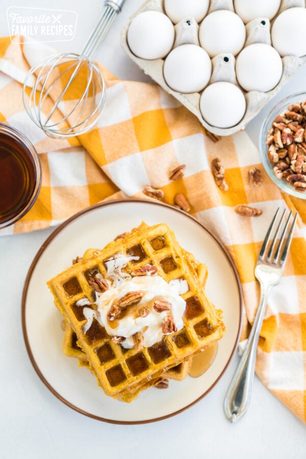 A stack of pumpkin waffles topped with whipped cream, pecans, and syrup.