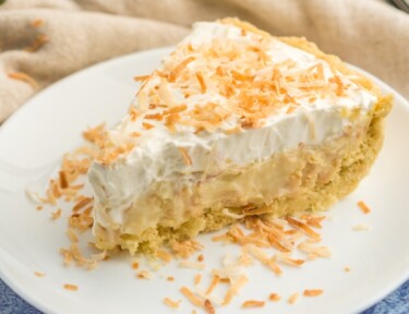 A slice of coconut cream pie on a plate topped with toasted coconut