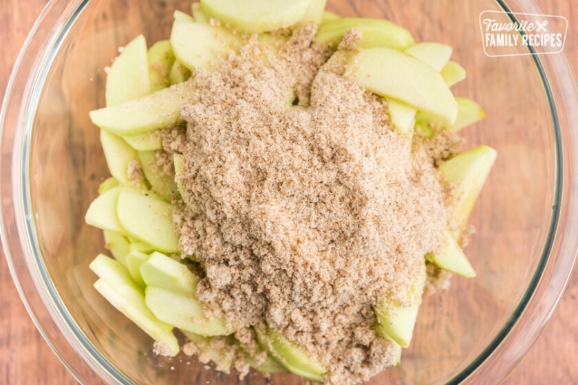 A clear bowl of sliced apples with sugar and seasoning on top