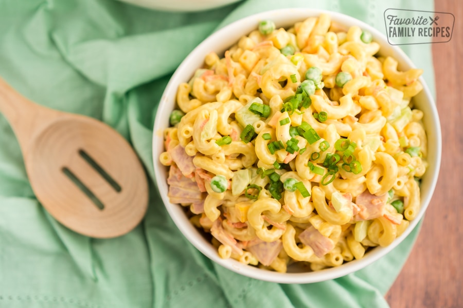 Macaroni salad in a white bowl with a wooden spoon and a green napkin
