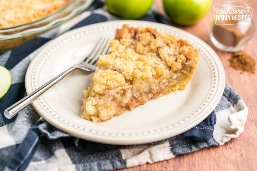 A slice of apple pie on a white plate with a fork on the side