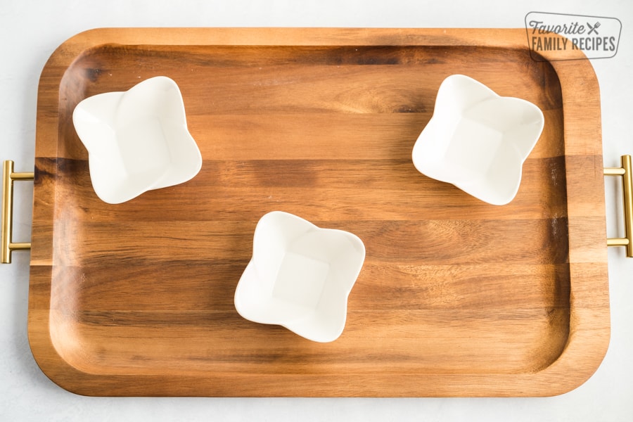 A wooden board with three small white bowls placed on it