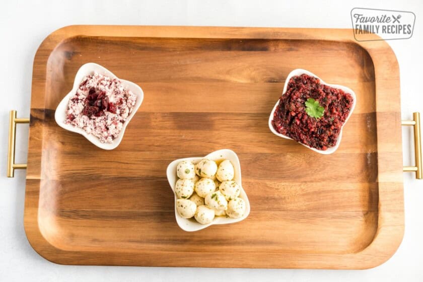 A wooden board with three small white bowls placed on it. Each filled with different dips.