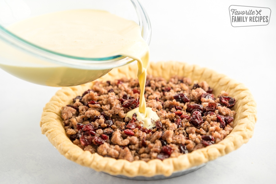 Eggs and cream being poured over a pie crust filled with sausage, cheese, and cranberries.