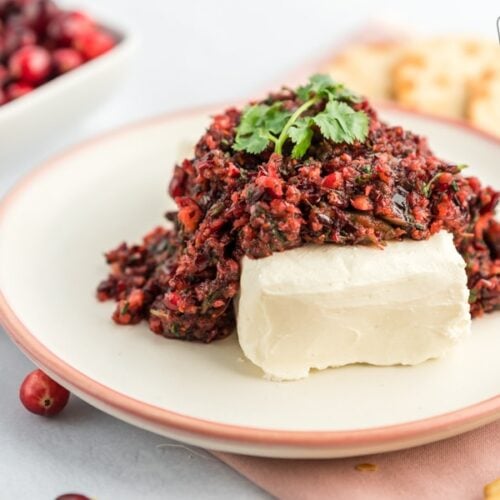 A plate with a block of cream cheese and cranberry salsa on it topped with some cilantro