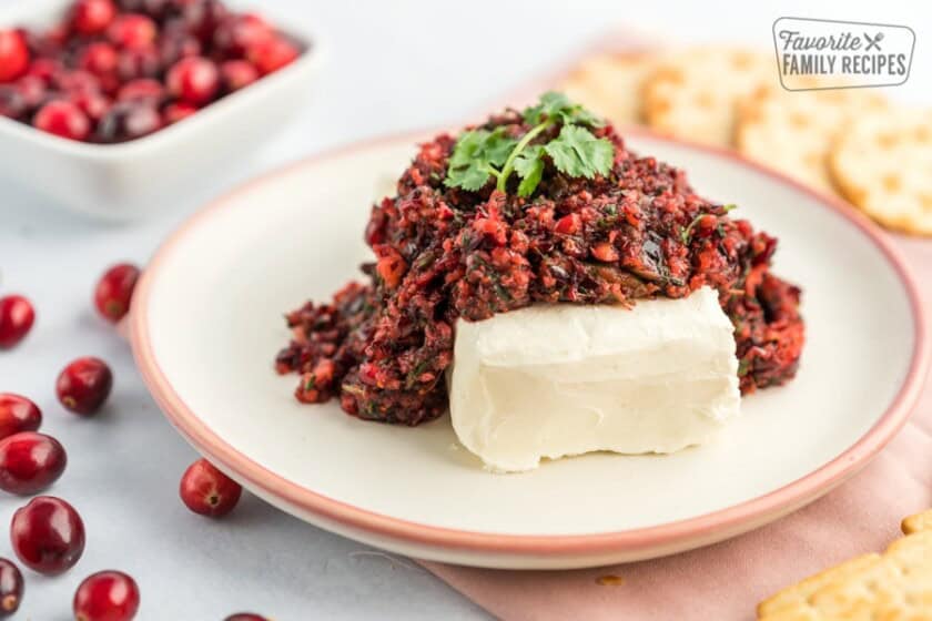 A plate with a block of cream cheese and cranberry salsa on it topped with some cilantro