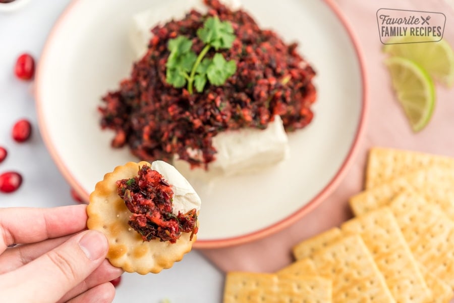 Cranberry Salsa is made with fresh ingredients and has an incredibly sweet and tangy flavor. This beautiful appetizer is perfect for Christmas and holiday parties. A cracker being dipped in cranberry salsa.
