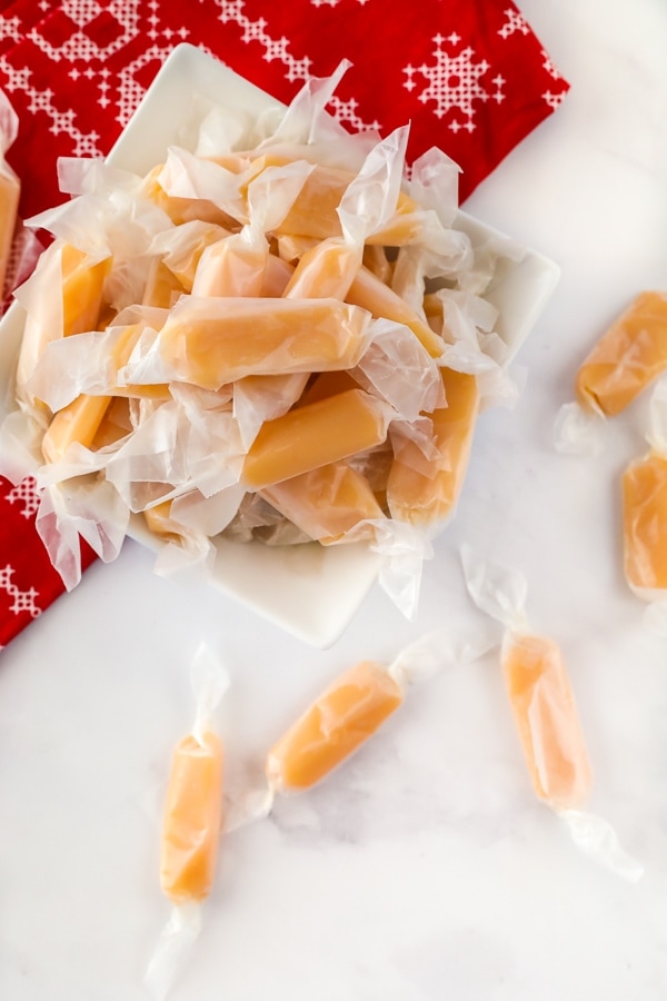 A dish of homemade caramels wrapped in wax paper.