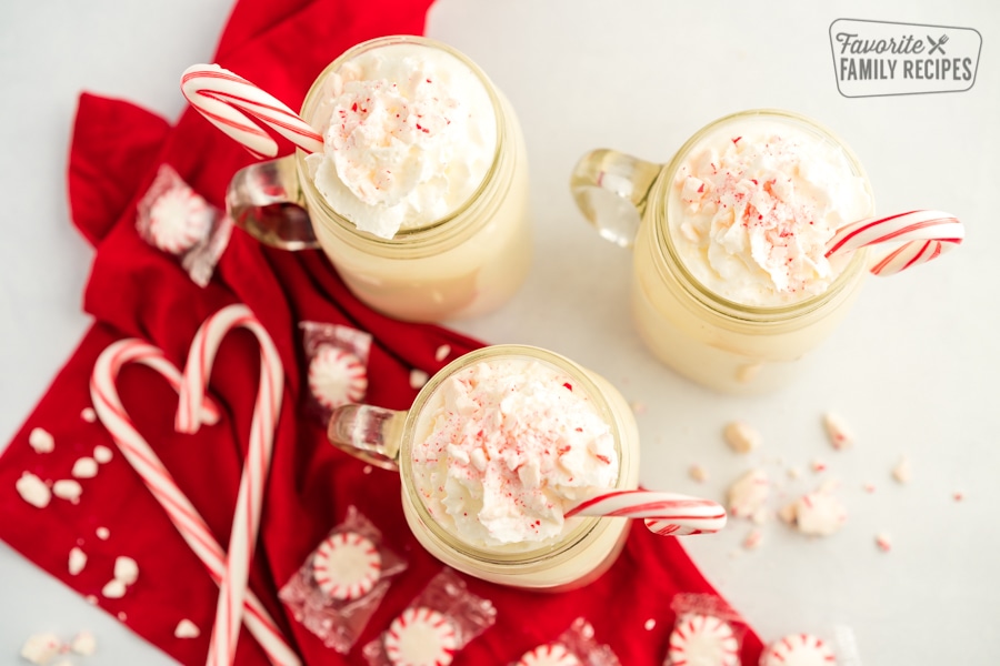 Three mugs of hot chocolate with whipped cream and crushed peppermints with a candy cane heart 