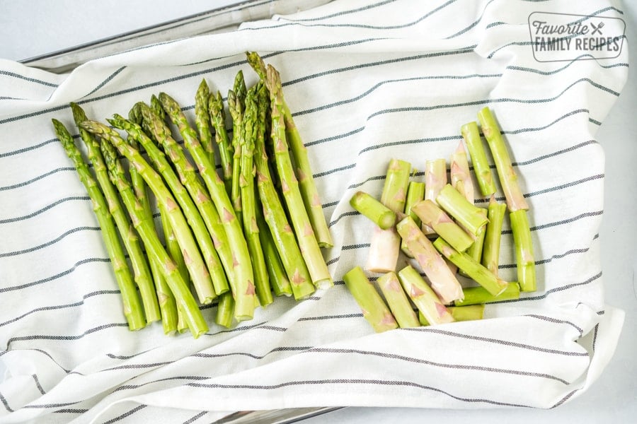 Oven Roasted Asparagus is a flavorful side dish for any meal. Topped with olive oil, garlic and cheese, they come out perfectly tender and crisp every time! Stack of trimmed asparagus on a striped dish cloth in preparation to make oven roasted asparagus.