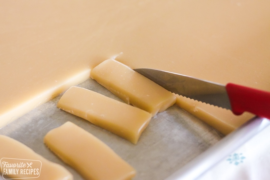 A pan of homemade caramels being sliced with a red knife.