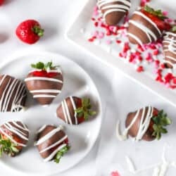 Chocolate covered strawberries on a white plate with other strawberries around them.