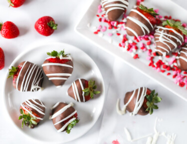 Chocolate covered strawberries on a white plate with other strawberries around them.