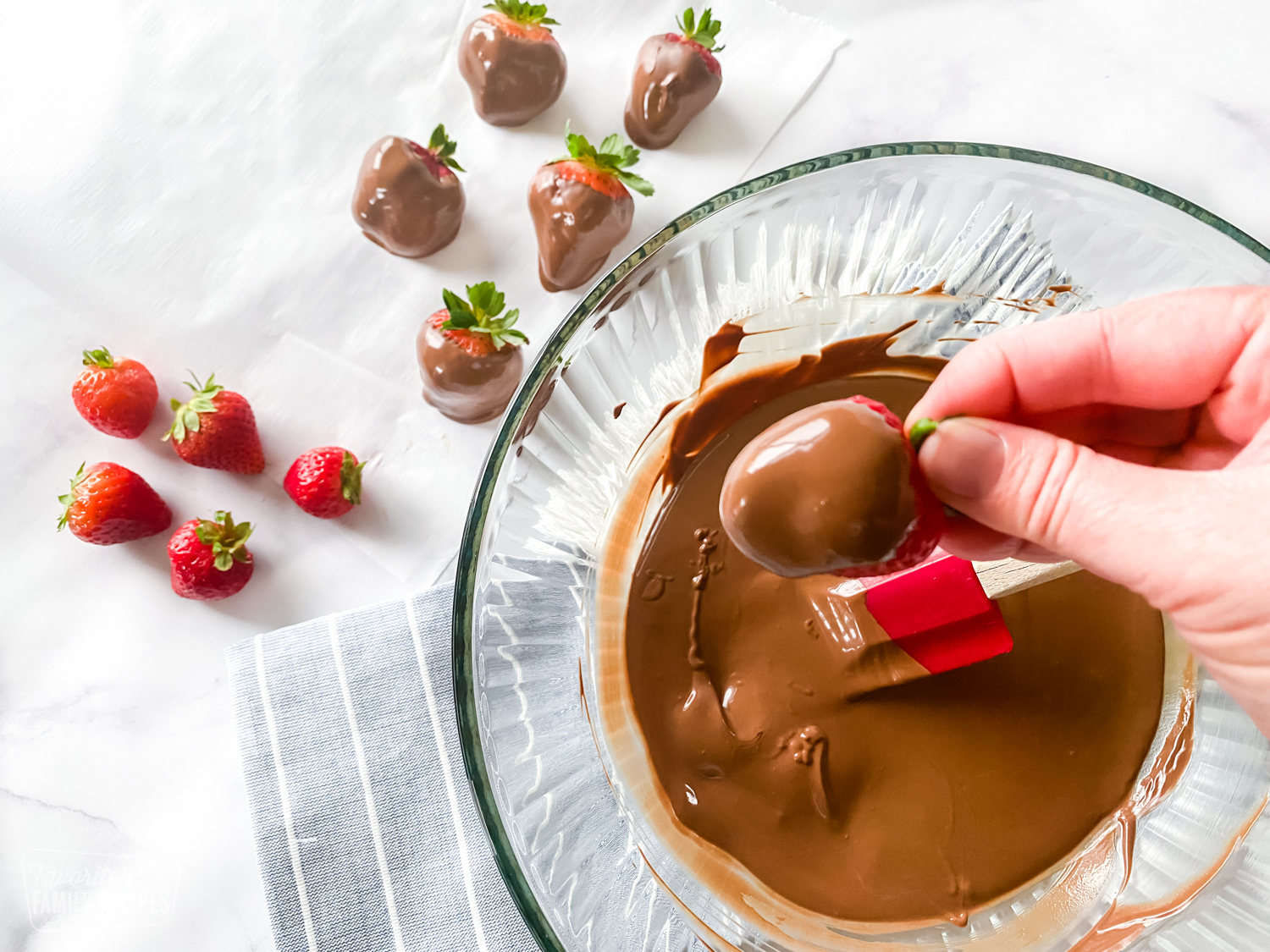 A chocolate covered strawberry being held with a hand.