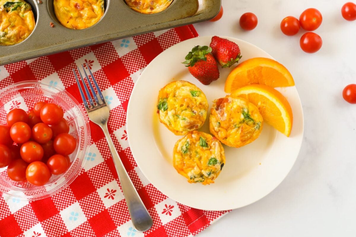 Breakfast egg muffins on a plate with fruit and tomatoes.