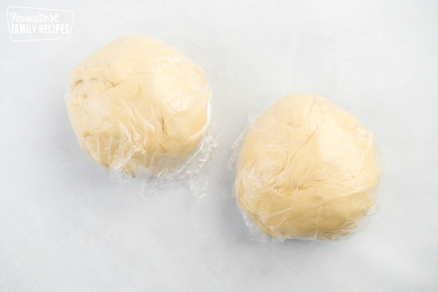 Two balls of homemade pizza dough wrapped in plastic wrap