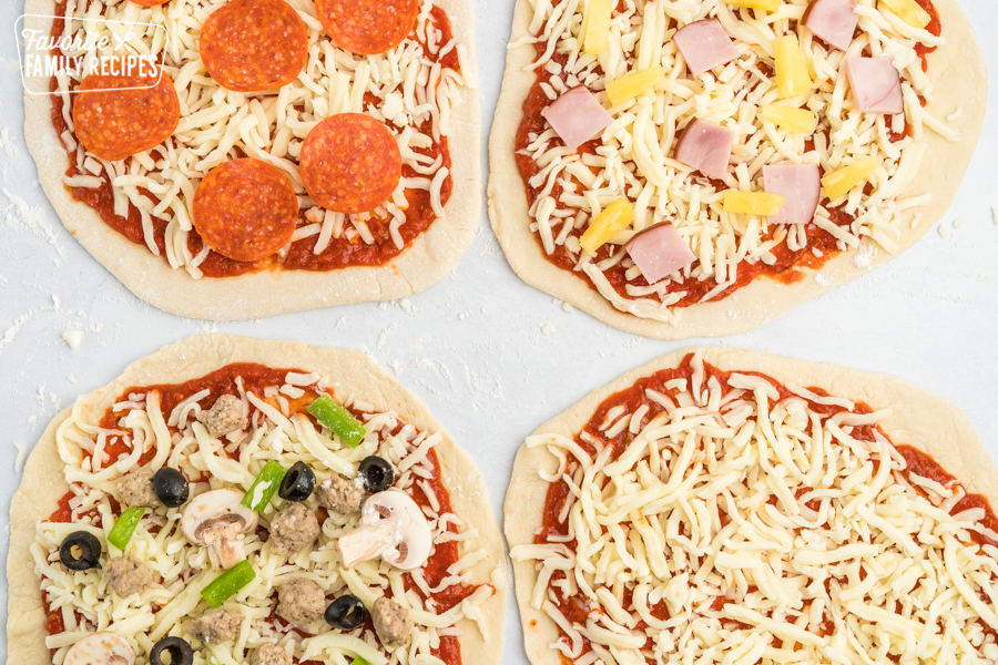 Four uncooked pizzas topped with different toppings