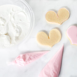 Royal icing in a bowl and in piping bags with sugar cookies