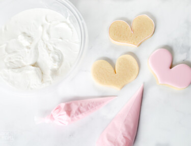 Royal icing in a bowl and in piping bags with sugar cookies