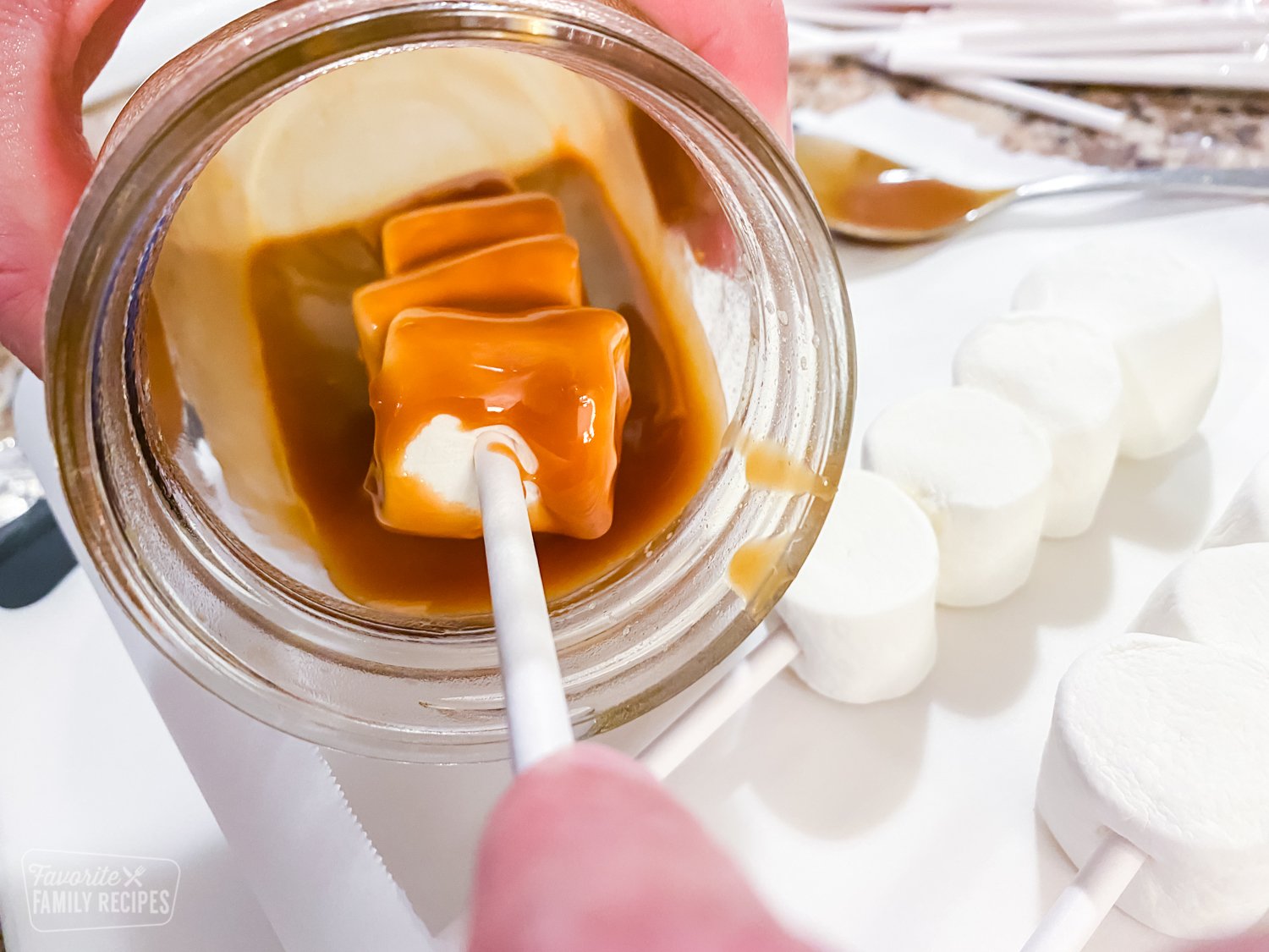 Marshmallows on a stick being dipped in caramel