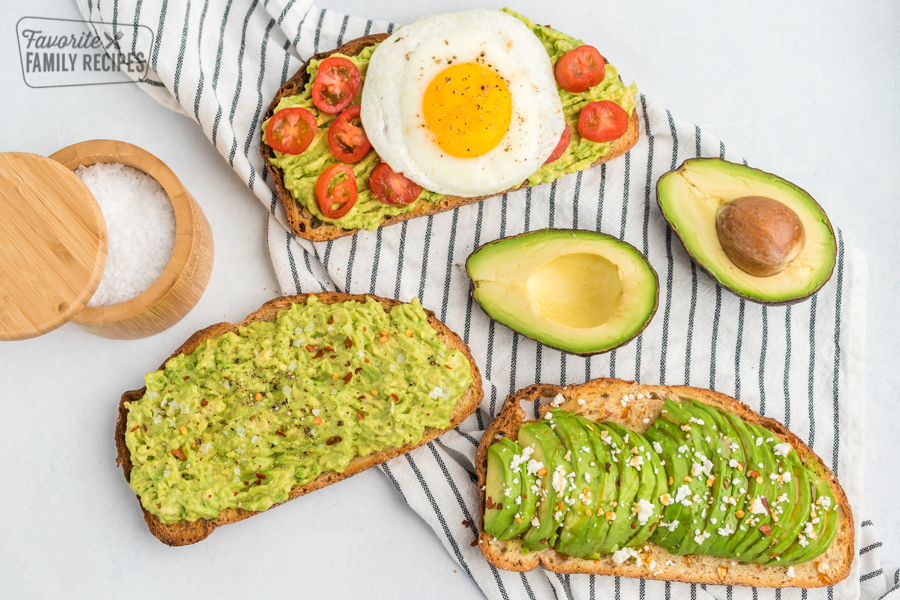 Three pieces of toast, one with mashed avocado, salt, and pepper, one with sliced avocado, feta, and honey, and one with mashed avocado, tomato, and a fried egg