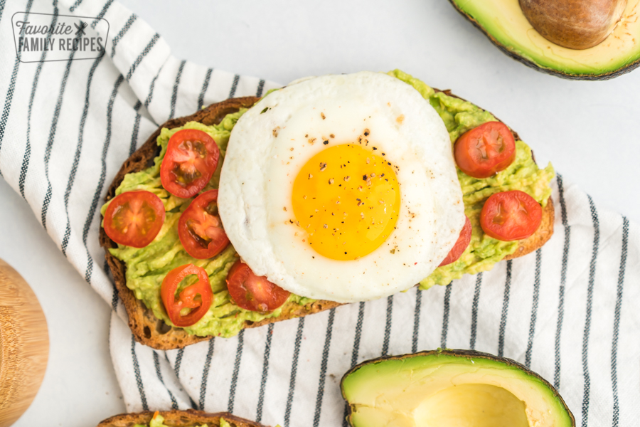A piece of toast with mashed avocados, sliced cherry tomatoes, and a fried egg